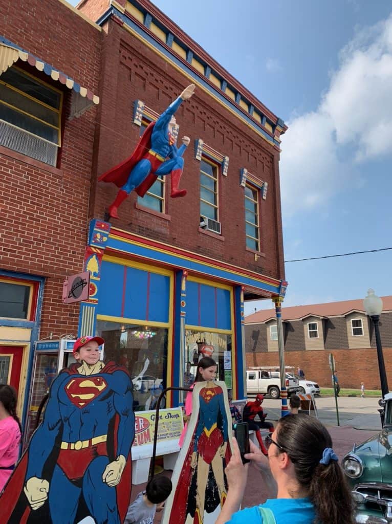 Two of our children place their heads in Superman and Superwoman cutouts. Spiderman sits on the bench and watches.