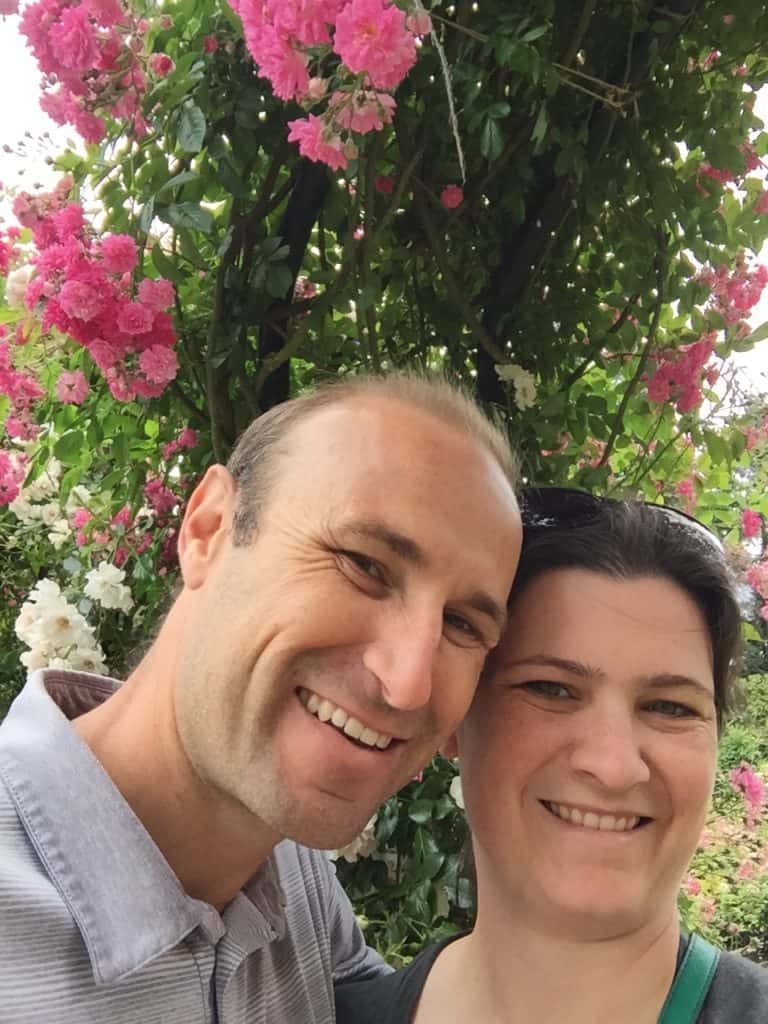 Husband and wife under a fclimbing rose in bloom.