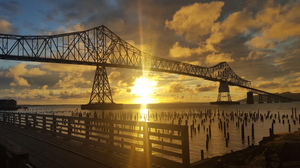 The sun ignites the horizon behind a bridge spanning the mighty Columbia River, near Lewis and Clark NHP.