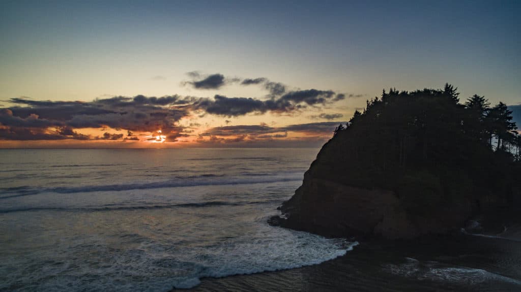 Foamy surf slowly wraps around Proposal Rock under the last rays of sunlight at Neskowin Beach.