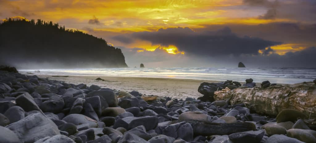 Mist rises over the sands and rounded rocks of Cape Meares Beach as the sunset sets the sky ablaze.