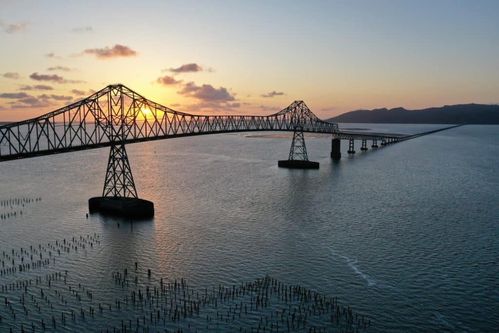 A tall steel bridge attempts to span the vast mouth of the Columbia River. The bridge bows down and becomes a lower river bridge about midway through the river.