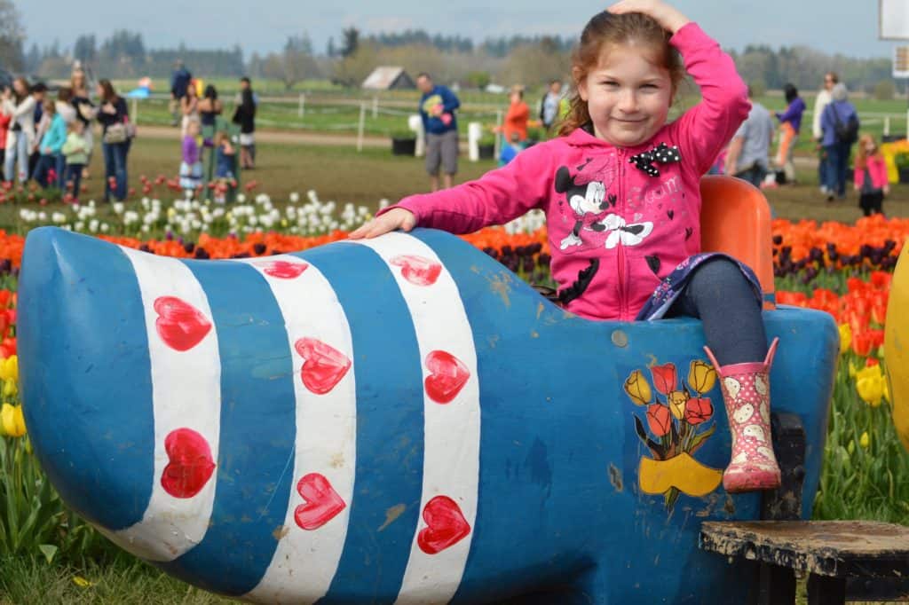 Little girl in giant wooden shoe in tulip field. Tulip Festival Oregon best time to go.