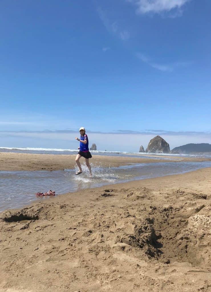 My daughter kicks up water as she splashes her way down Cannon Beach. Haystack Rock stands in the background.