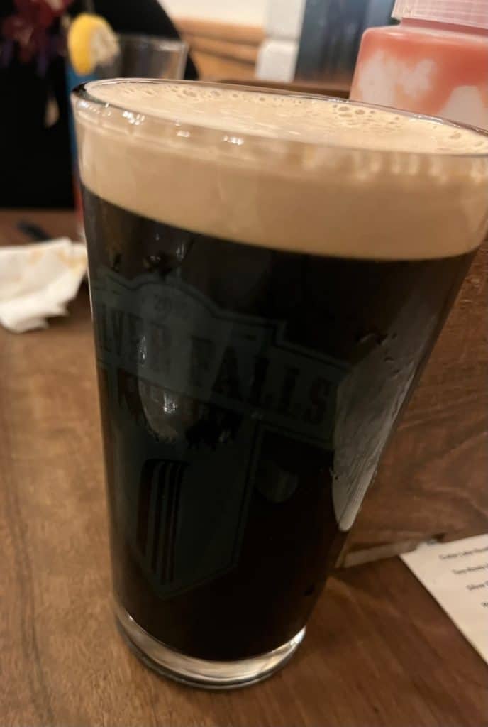 A soft tan head of foam tops a tall, dark glass of Top Knot Irish Stout.