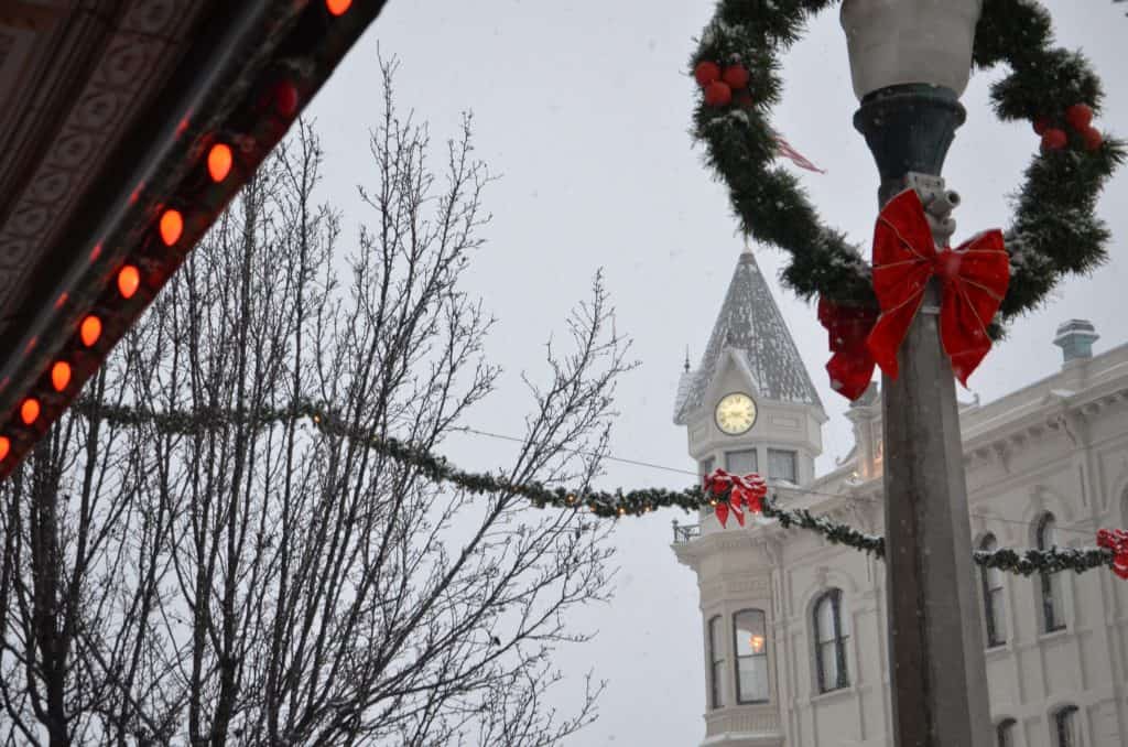 Wreaths, lights, and bows decorate snowy victorian buildings in the historic town of Baker City. 