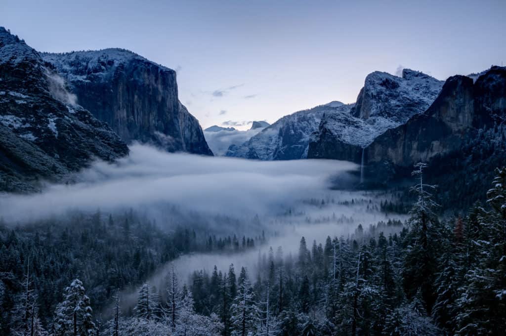 Snow-covered crags rule over the misty valley floor at Yosemite National Park. Yosemite National Park is one of the best national parks to visit in November and December.