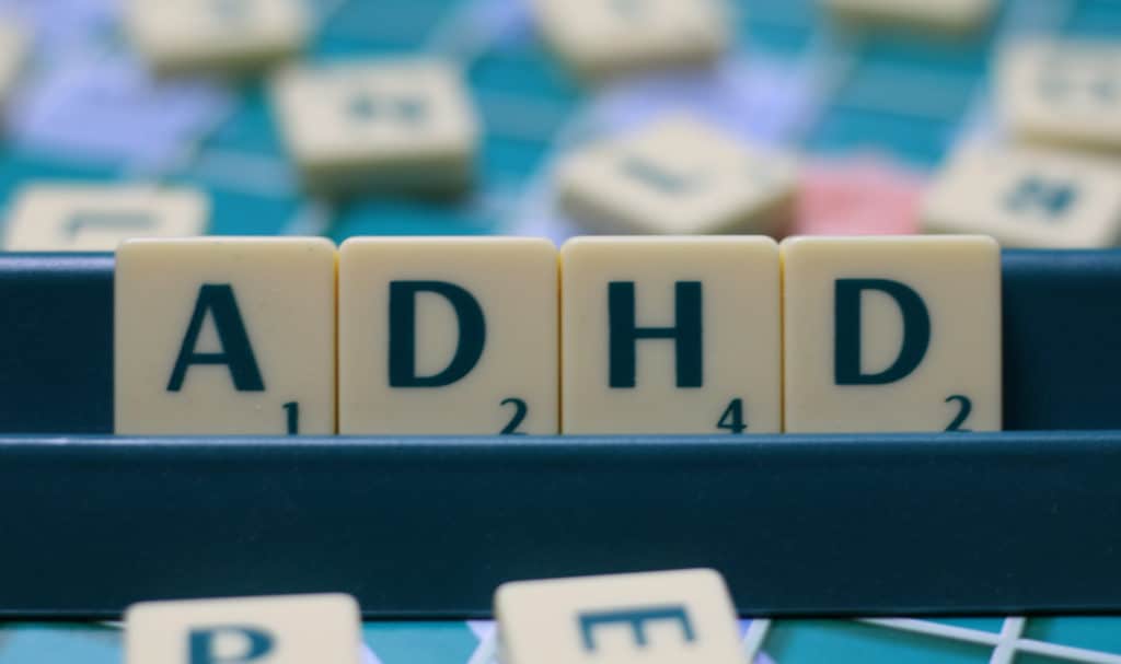 Four Scrabble tiles stand in a tile holder and spell "ADHD".
