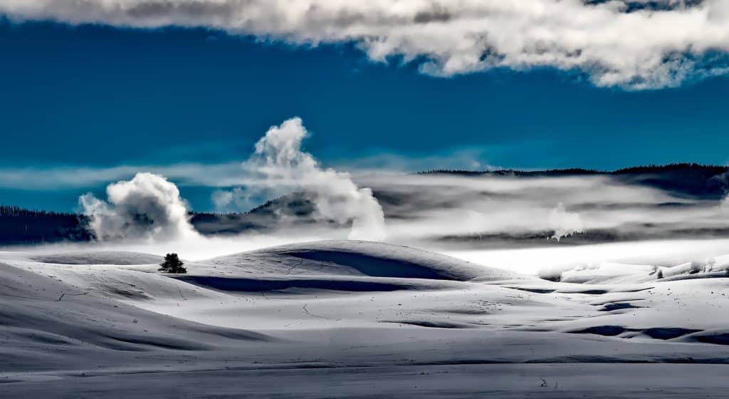 Steam rises from geysers hidden under blankets of snow at Yellowstone National Park. Yellowstone National Park is one of the best national parks to visit in November and December.