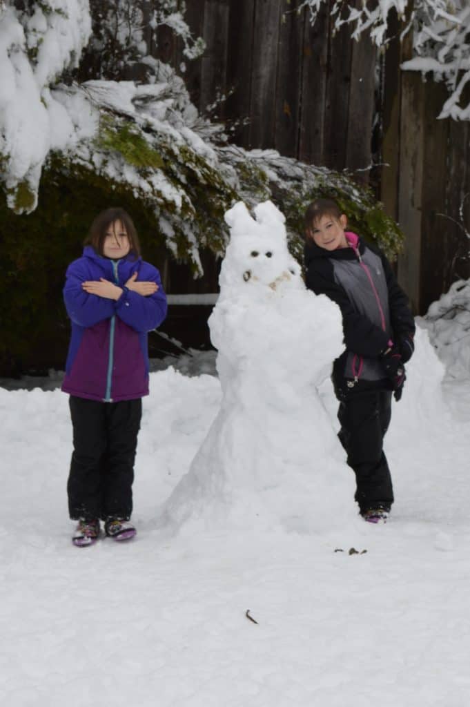Girls standing in snow with snowman.