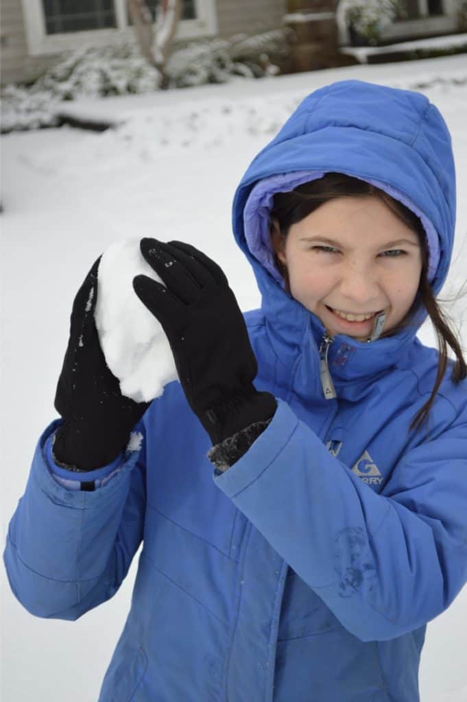 Girl holding a snowball ready to throw. Family Christmas bucket list.