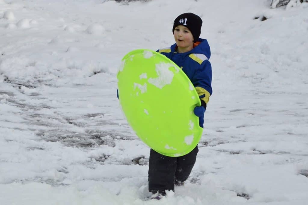 Boy holding sled in the snow. Family Christmas bucket list.