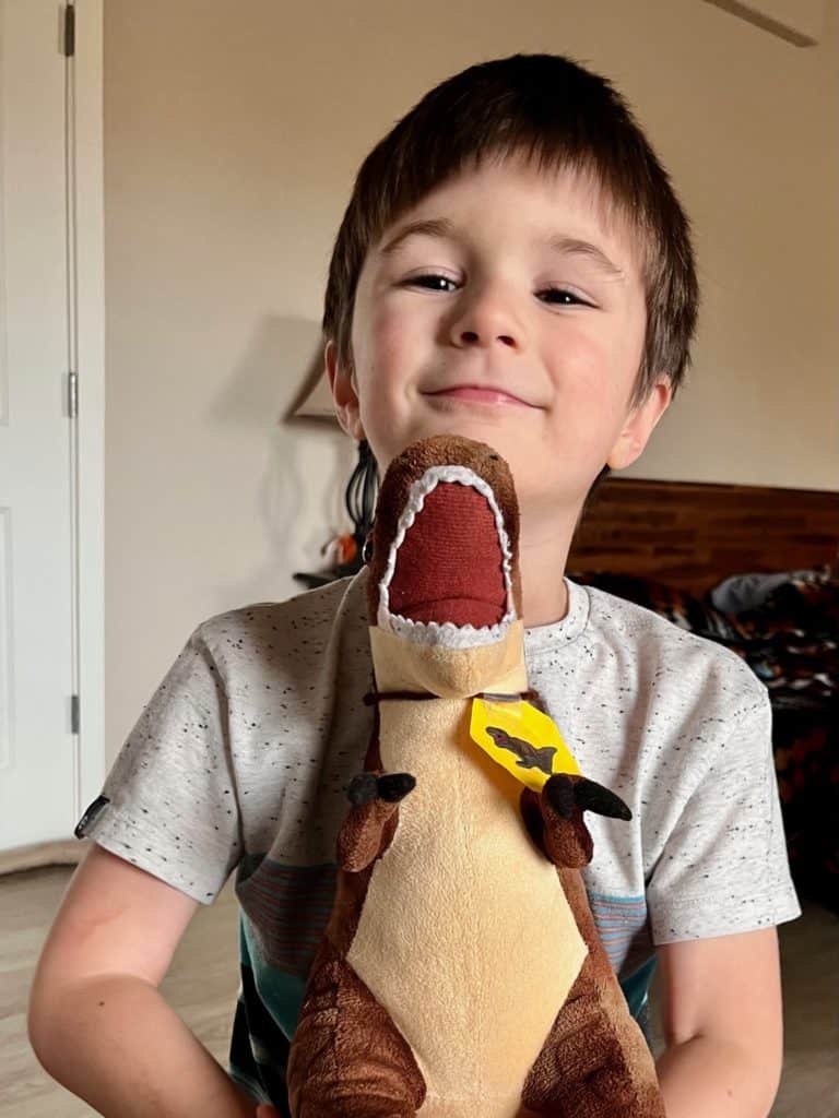 Boy holding stuffed T. rex dinosaur. 
