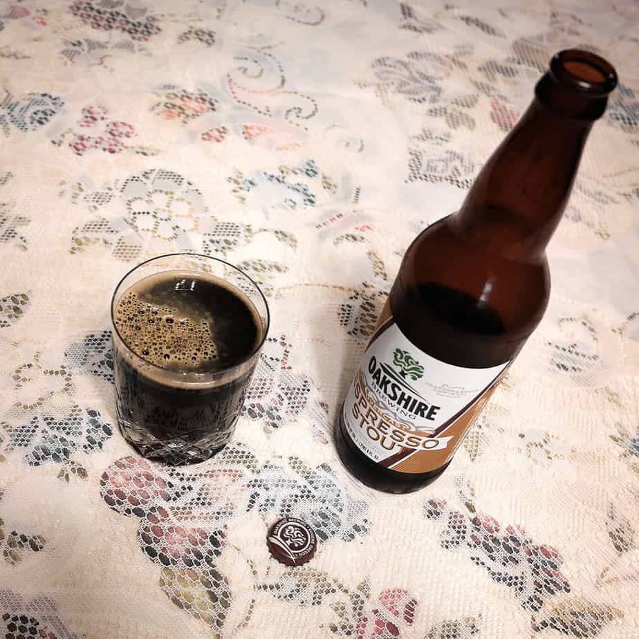 A glass of dark Oakshire Espresso Stout sits on top of an old fashioned lace tablecloth.
