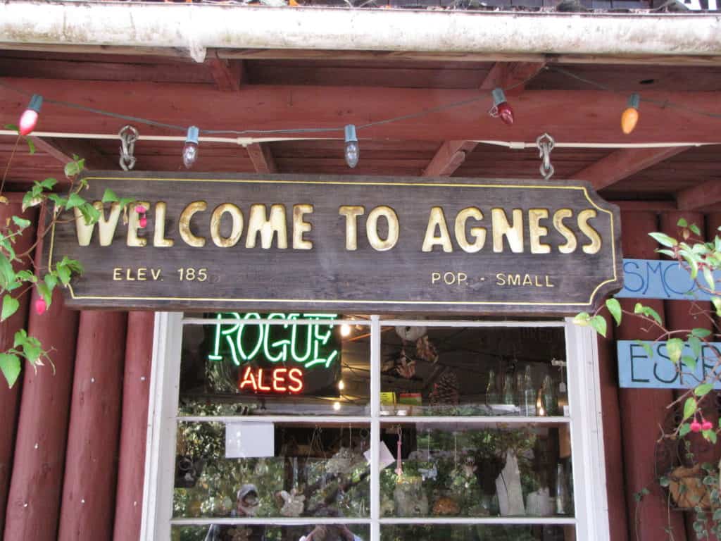 A rustic market sign says "Welcome to Agnes, Elev. 185, Pop. Small". 
