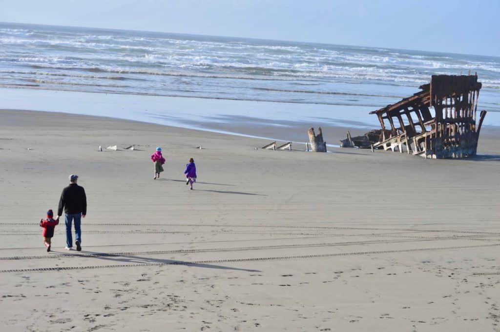 Me and my children walk toward the rusted remains of the Peter Iredale Shipwreck at Fort Stevens State Park. Fort Stevens SP is a great place to go when traveling the Oregon Coast with kids.