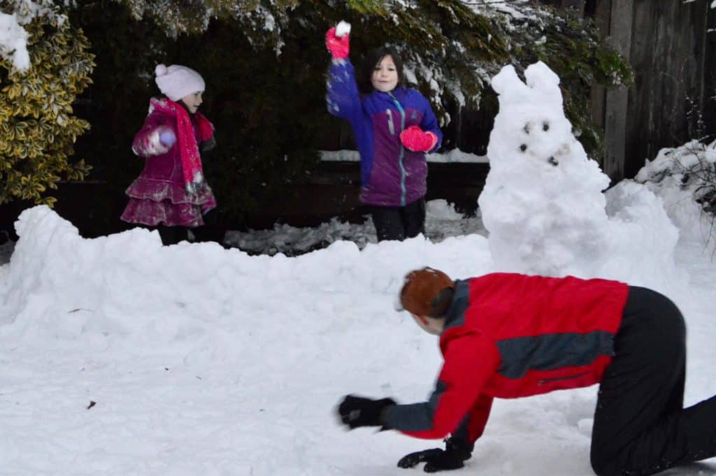 Dad and girls having a snowball fight with a snow fort.  Winter activities for teens