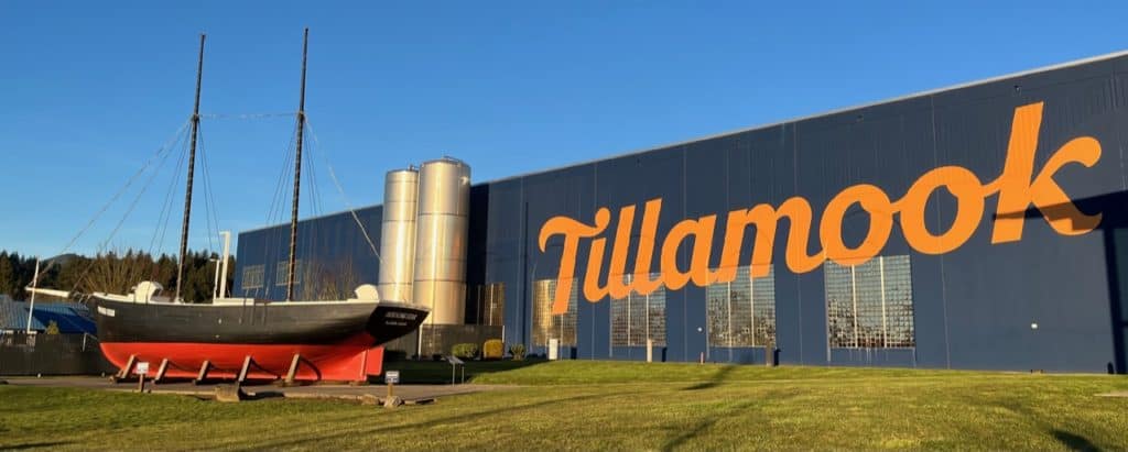 A historic ship sits just outside the big, blue Tillamook Creamery Factory building. Tillamook Creamery is one of the funnest attractions to visit when touring the Oregon Coast with kids.