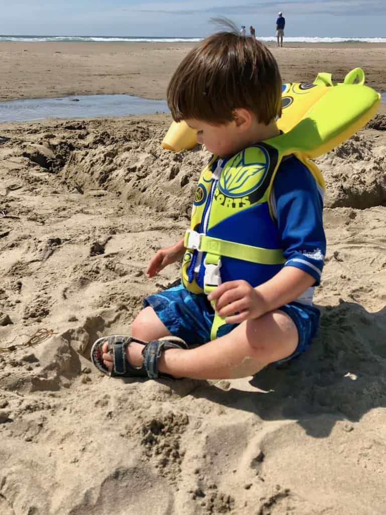 Boy in life jacket at the beach. Beach packing list family.
