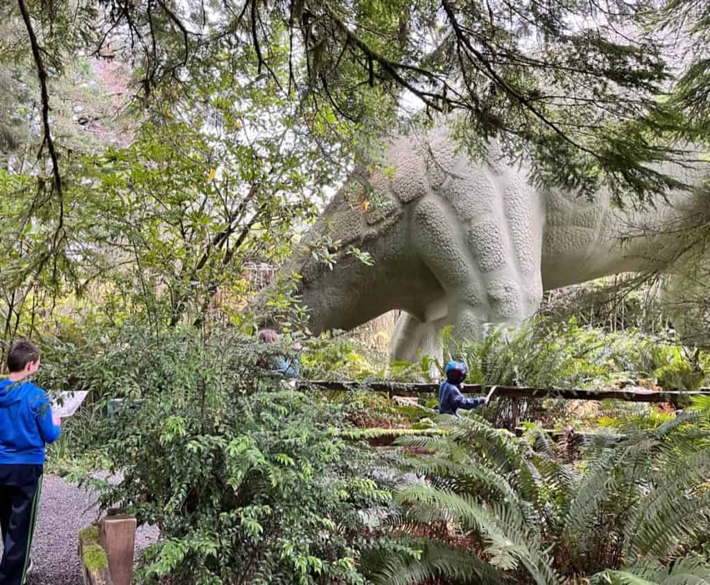 My children approach the hindquarters of a brachiosaur statue at Prehistoric Gardens. Prehistoric Gardens is a fun stop to do when visiting the Oregon Coast with kids.