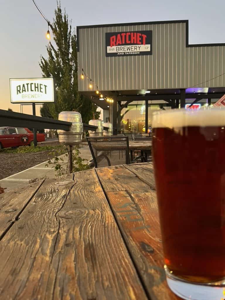 An amber ale stands on a table in front of Rachet Brewery.