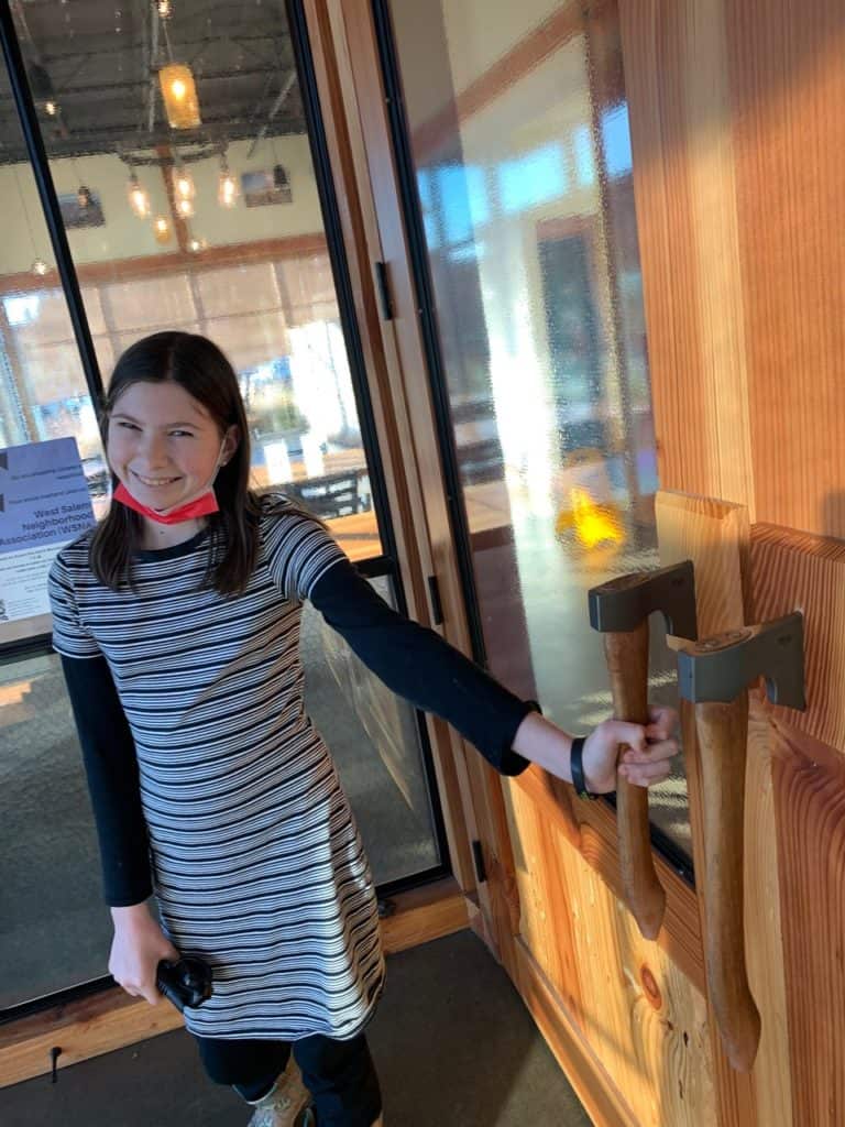 My daughter stands smiling and holding one of the axe door handles at Gilgamesh Brewery. Gilgamesh is one of many breweries Salem Oregon.