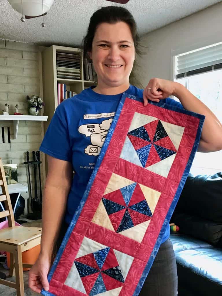 Mom holding a quilted table runner. Hobby items make great gifts for homeschool moms.