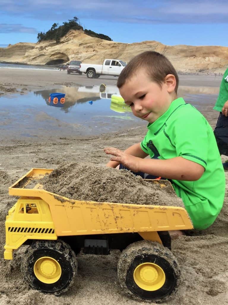 Boy playing with dump truck at the beach. Beach packing list family.