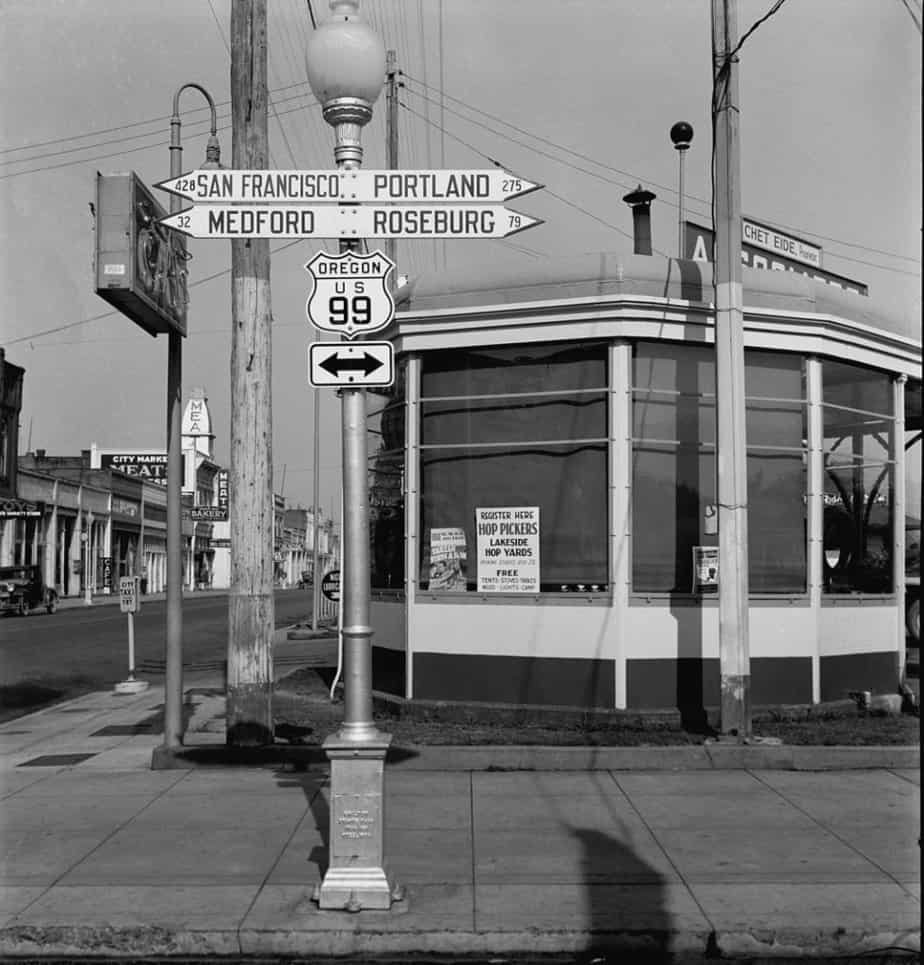 A historic, black and white photo shows a US 99 Highway sign from Grants Pass Oregon.