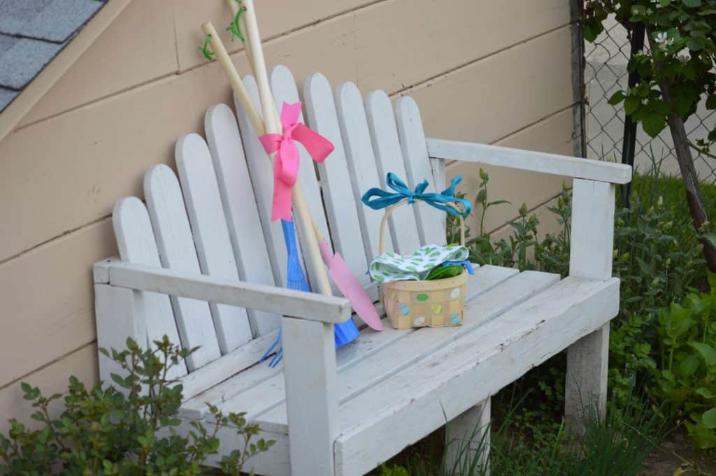 White bench in garden with Easter basket and garden tools. non candy ideas for easter baskets