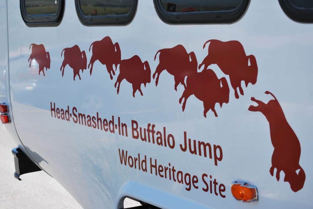 A shuttle at Head-Smashed-In Buffalo Jump bears the attractions logo. The logo consists of a herd of red buffalo running off a cliff. The front buffalo is taking a nose dive.