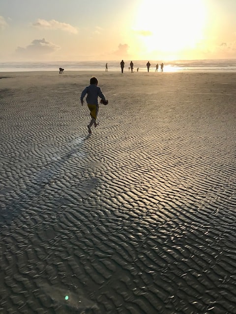 Boy running towards sunset at ocean.