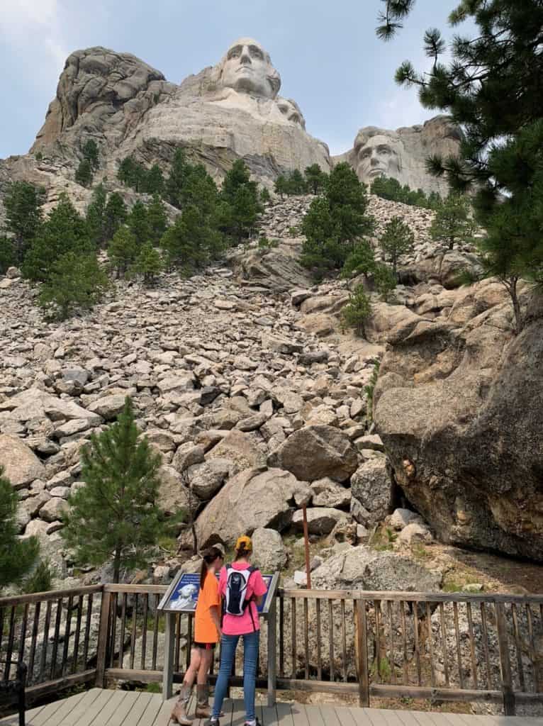 Two children read an informative display under the watchful gaze of Mount Rushmore at Mount Rushmore National Memorial.