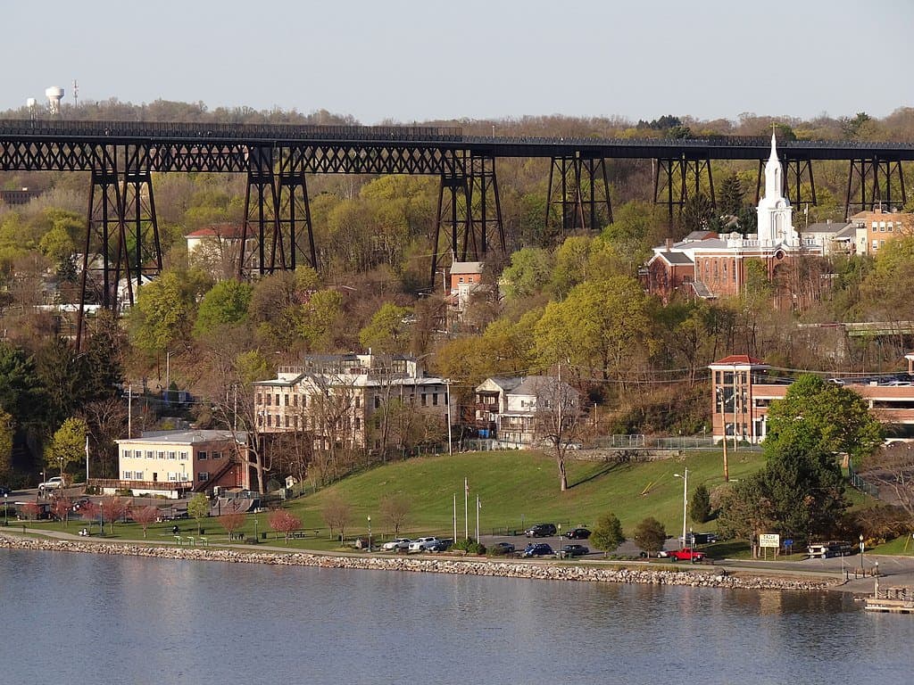 The Walkway Over the Hudson towers over historic riverfront buildings and church steeple. The Walkway Over the Hudson is one of the highest bridges in the US.