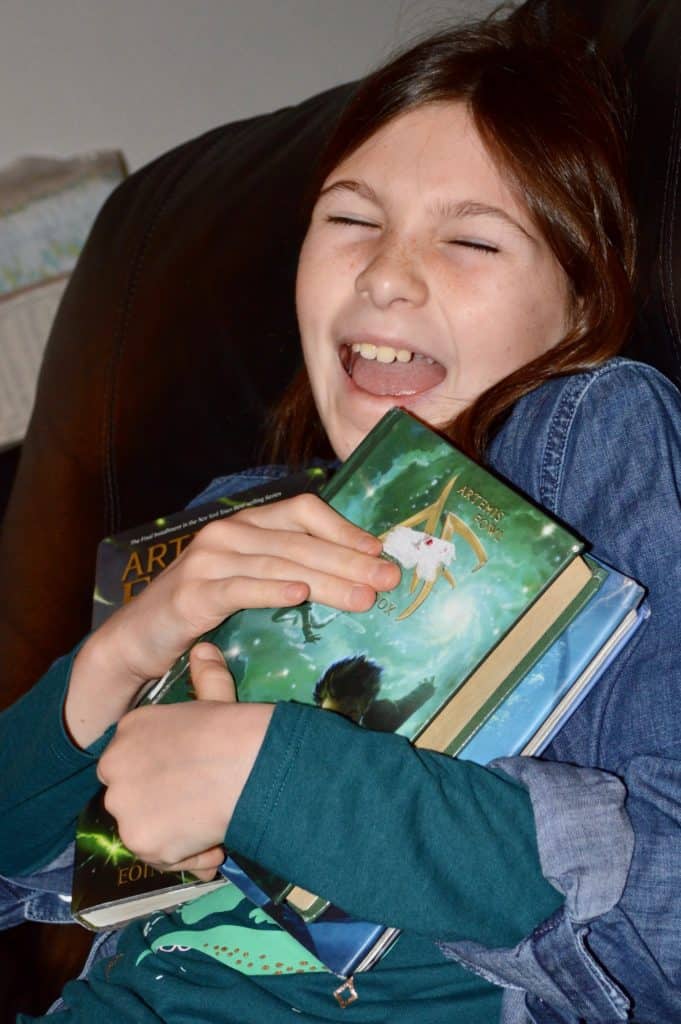 Girl excited holding Artemis Fowl books. Great science fiction books for 5th graders.