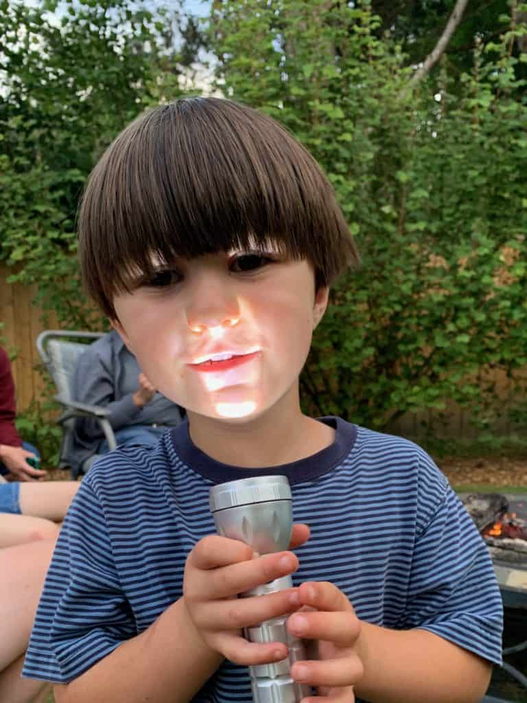 Boy with flashlight shining on face. Camping gifts for kids