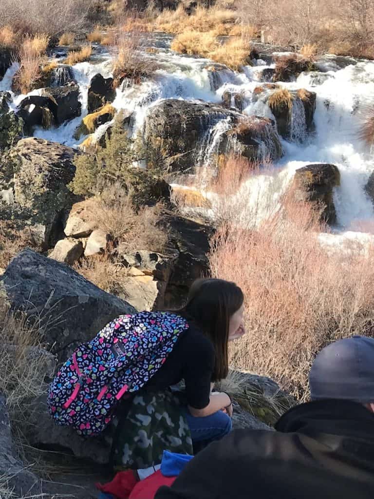 Girl watching a waterfall with a backpack on back. Camping gifts for kids and teens.