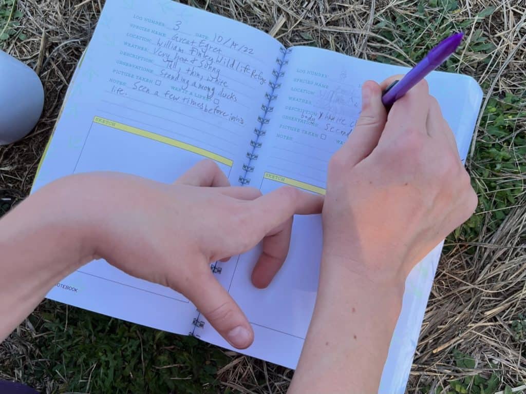 Hands writing in the Nature Journal pages from the North American Field Guide for birds. camping gifts for kids