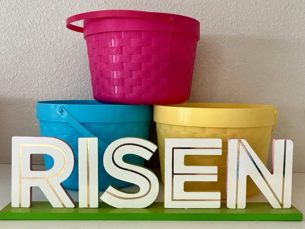 White wooden word art "RISEN" with blue, pink and yellow plastic Easter tubs behind