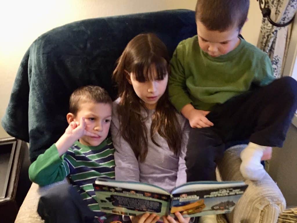 Girl in armchair reading book to boys. Great science fiction books for 5th graders.