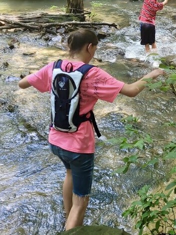 Girl crossing stream with hydration backpack on. Camping gifts for kids and teens.