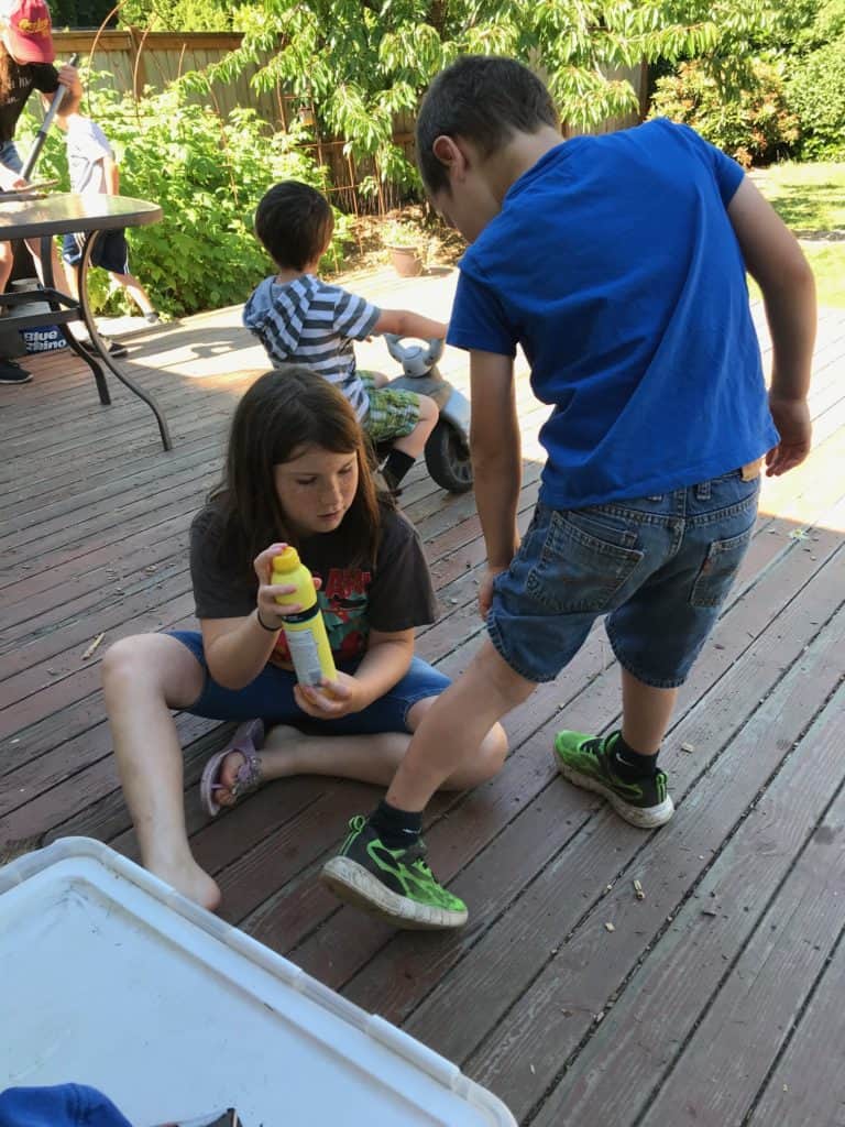 Girl helping boy spray sunblock on his leg. camping gifts for kids