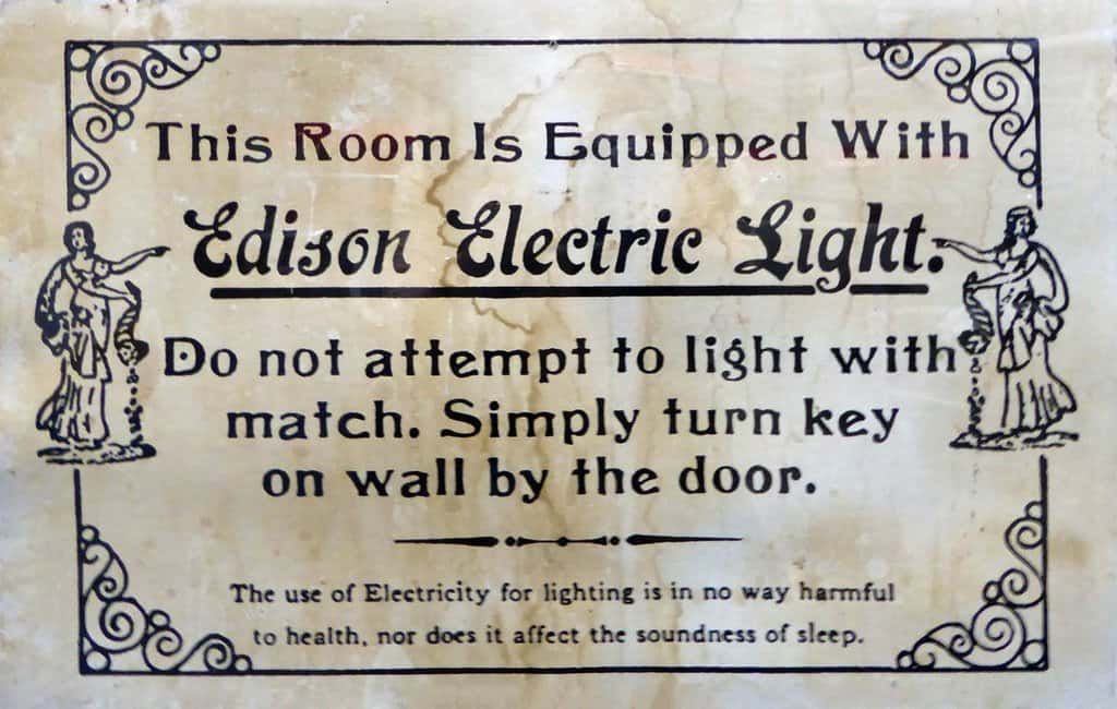 An antique Edison Electric sign says "This room is equipped with Edison Electric Light. Do not attempt to light with match. Simply turn key on wall by the door."
