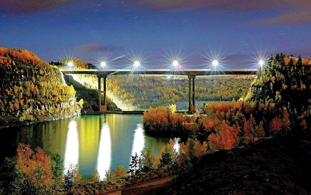 A nighttime shot of the Thomas Rukavina Memorial Bridge shows the bridge lighting up the waters below it.
