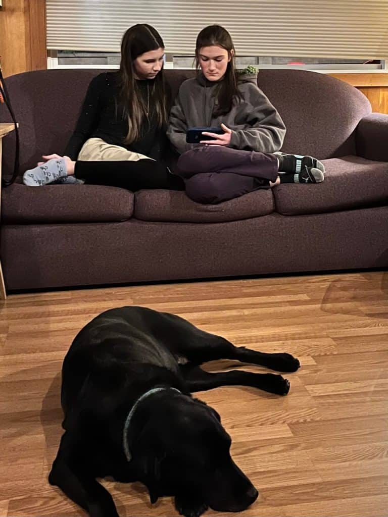 Teens watching a phone on a couch with Labrador on floor in front. Repairing a Parenting mistake with teens.