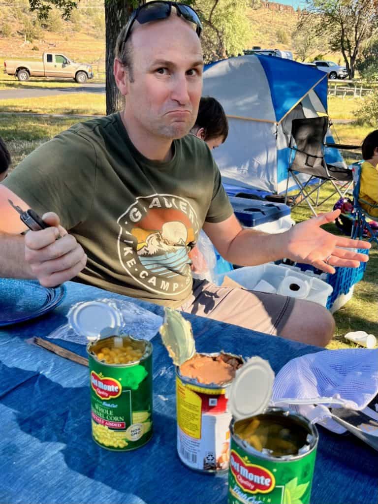 Man making a face with open cans in front that were opened badly.
