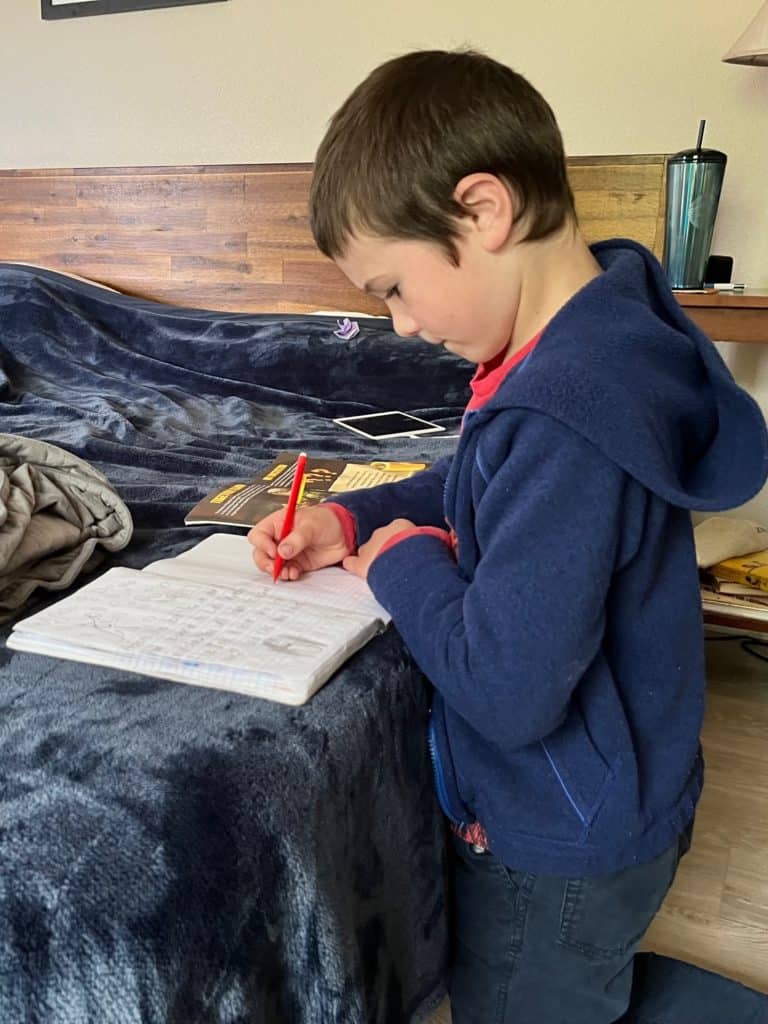 Boy working on writing on a bed. Calming ADHD bedroom ideas.