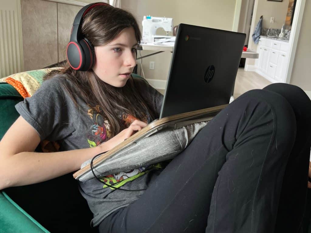 Girl working on a laptop with lap desk. Calming ADHD bedroom ideas.