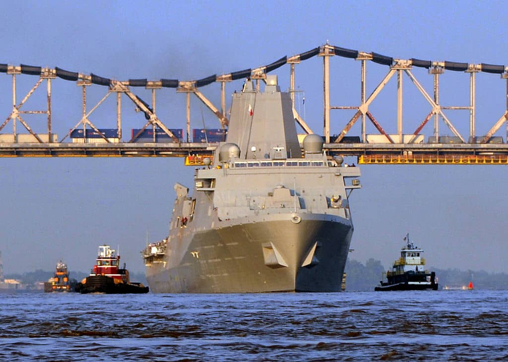 An enormous Navy Ship passes under the Huey P. Long Bridge. The Huey P. Long Bridge is one of the highest bridges in the US.