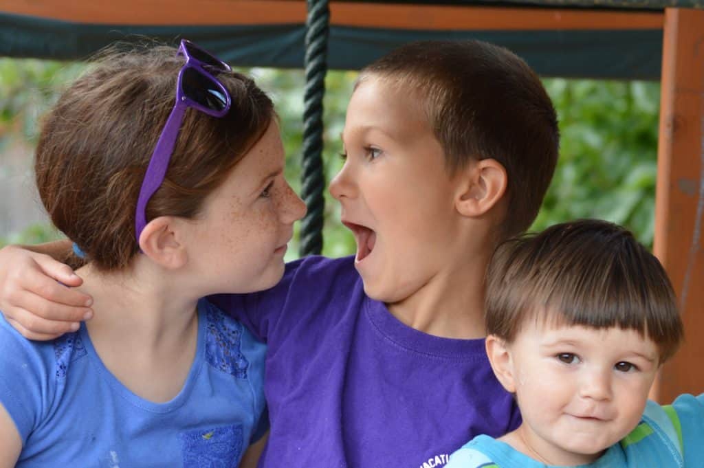 Girl and boy looking at each other with toddler in front. Encouraging good sibling relationships.